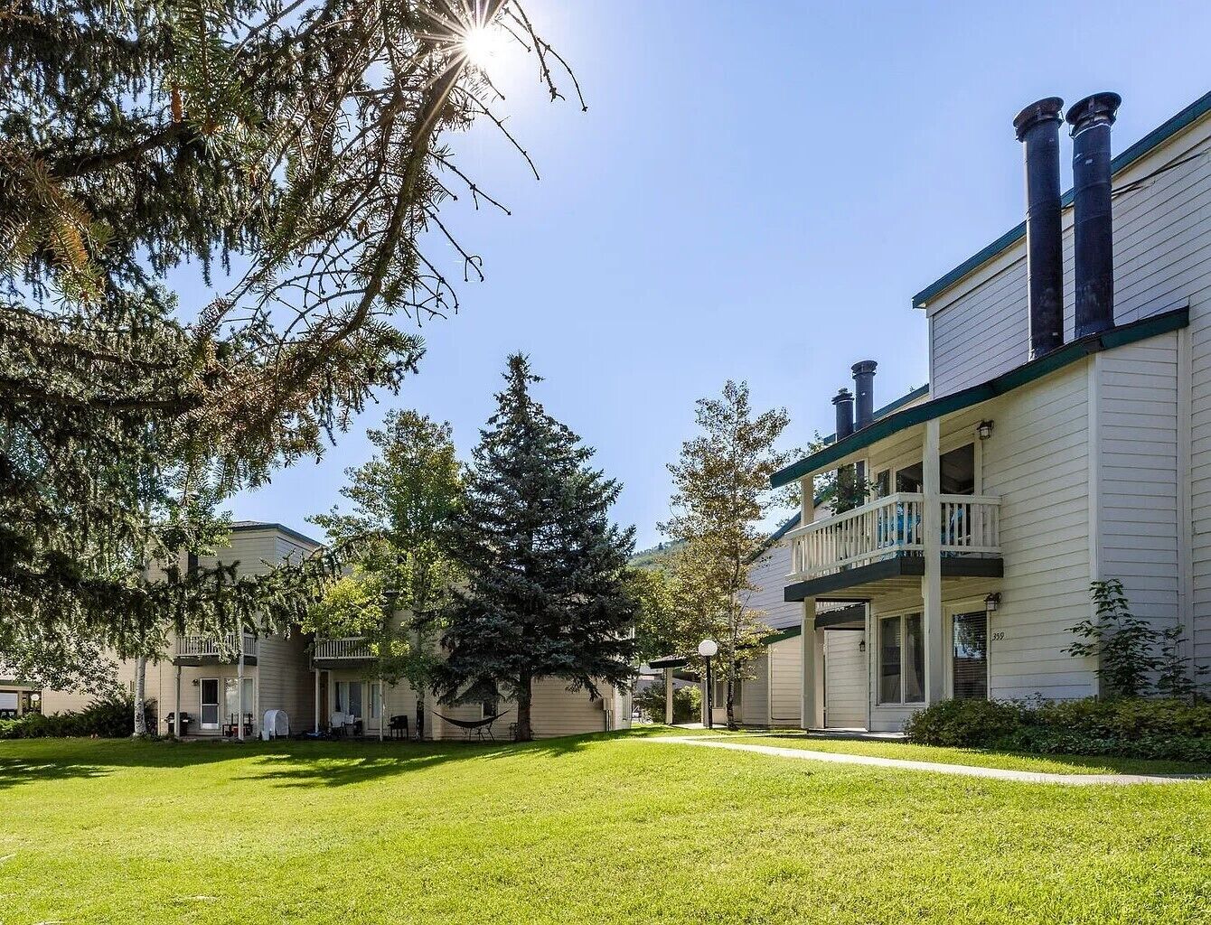 A two-story building with a balcony on the second floor, a covered patio, and a well-maintained lawn.
