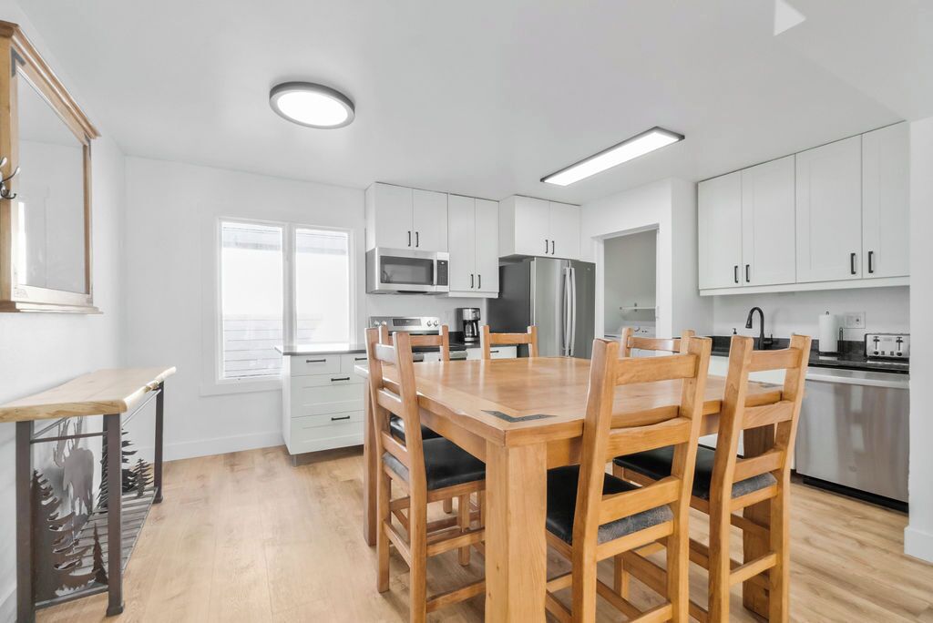 Une cuisine moderne avec des meubles blancs, une table à manger en bois et un micro-ondes encastré.