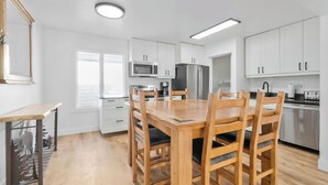 A modern kitchen with white cabinets, a wooden dining table, and a built-in microwave.