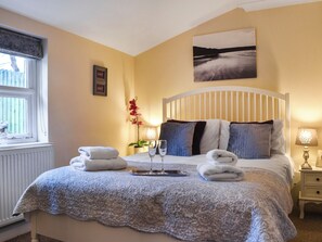 A neatly made bed with towels, a bedside table with a lamp, and a window with blinds.