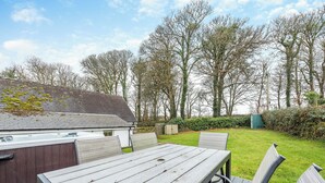Une table et des chaises en bois dans un jardin, avec une maison en arrière-plan.