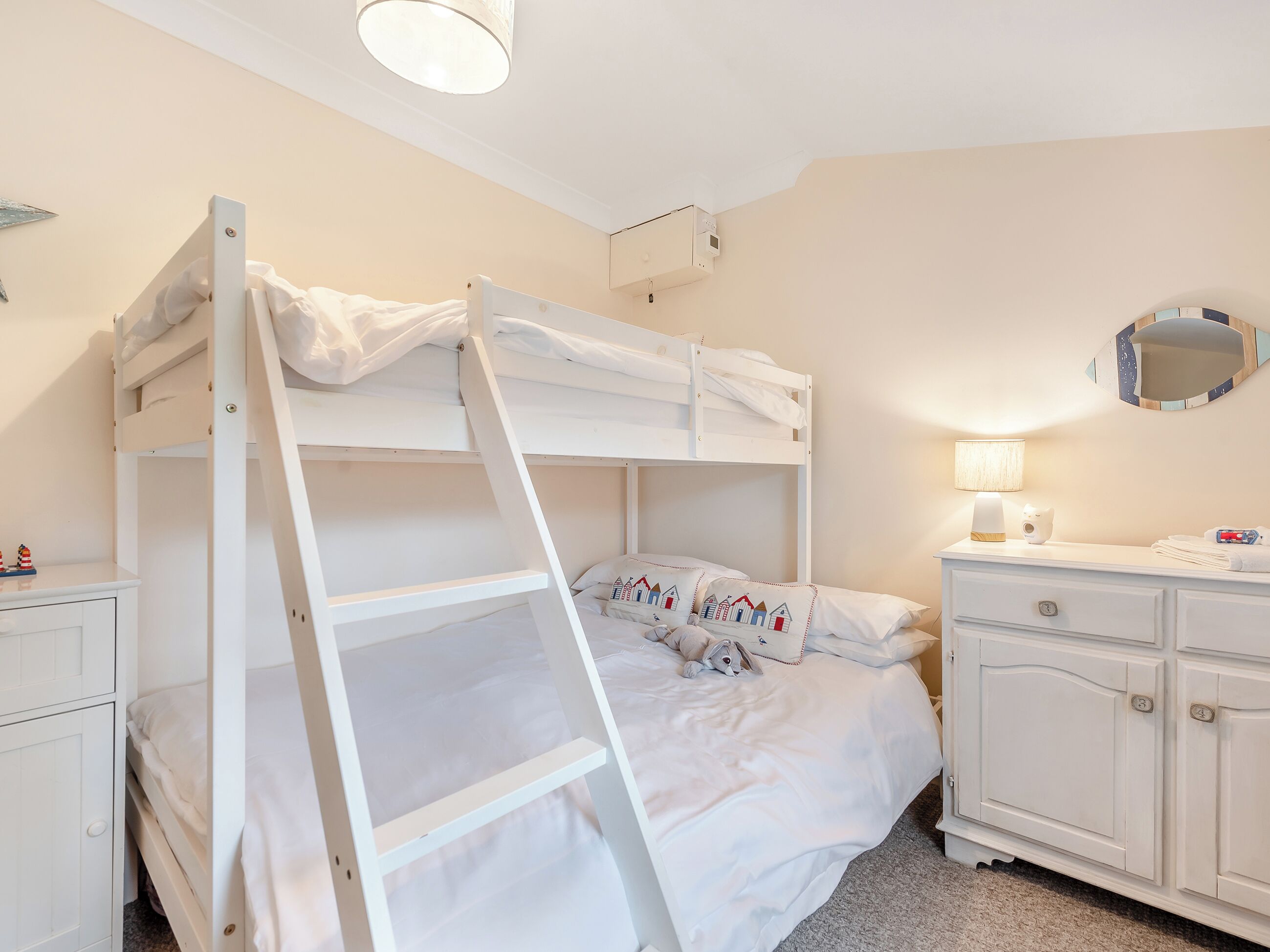 A bunk bed room with a ladder, a bedside table with a lamp, and a dresser.
