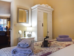 A neatly made bed with folded towels, a bedside table with a lamp, a mirror, and a decorative vase. - 3 bedroom accommodation in Roch (Roch)