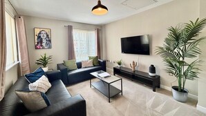 En moderne stue med en sort sofa, et sofabord, et fladskærms-TV og en loftventilator.