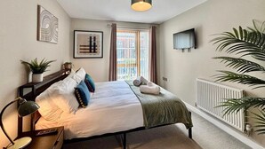 Et soveværelse med seng, skrivebord med lampe, radiator og et vindue med gardiner.