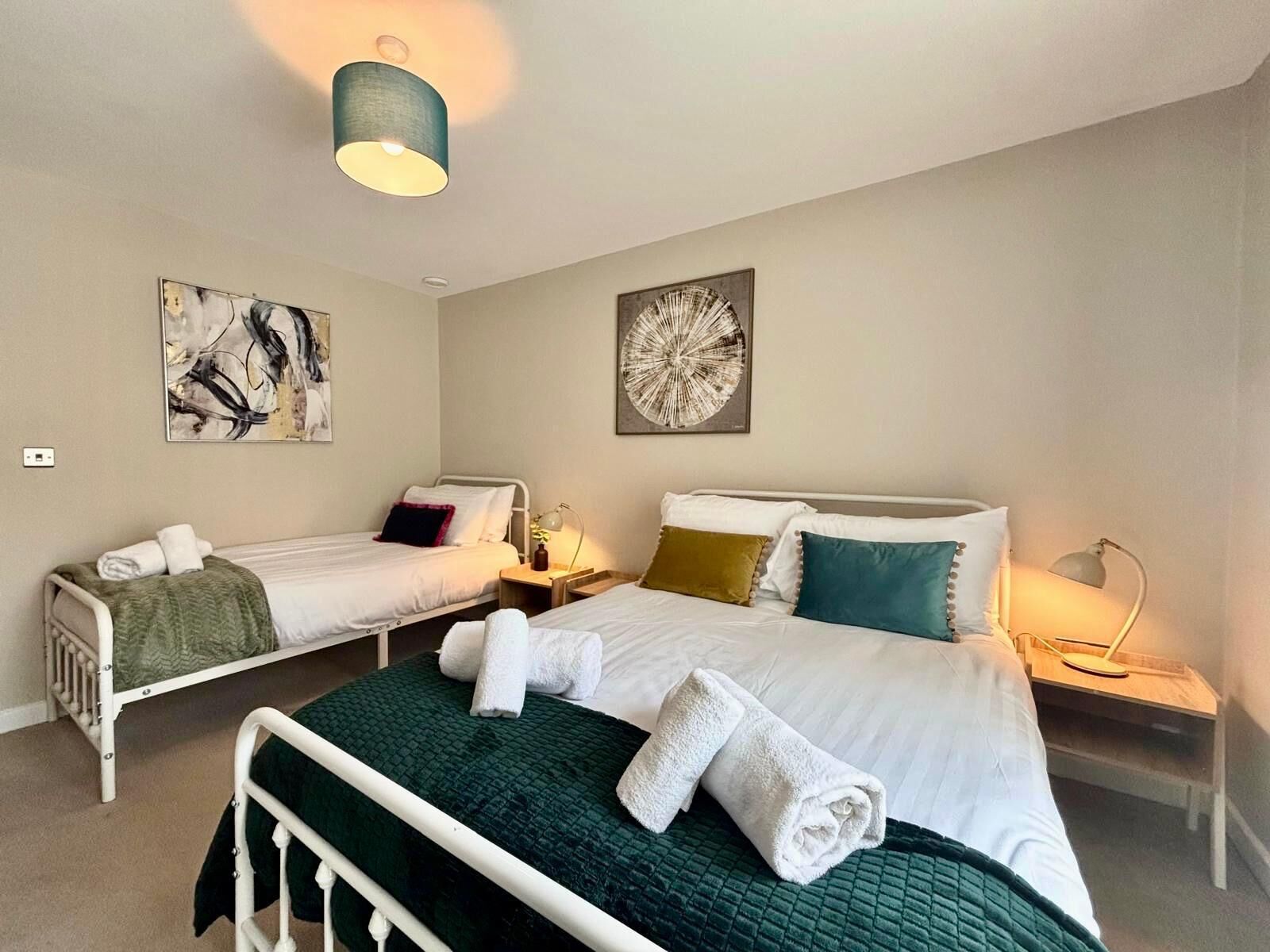 Ett hotellrum med två enkelsängar, en stor säng och ett skrivbord. Det finns två konstverk som hänger på väggen, en taklampa och ett nattduksbord med en lampa.