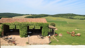 A covered outdoor seating area with tables and chairs, surrounded by a lush green landscape and hills in the background. - Nice Apartment in Guasticce With Pool (Collesalvetti)