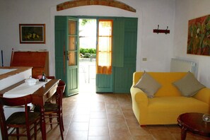 A room with a dining table, chairs, a yellow sofa, and an open door leading outside. - Nice Apartment in Guasticce With Pool (Collesalvetti)