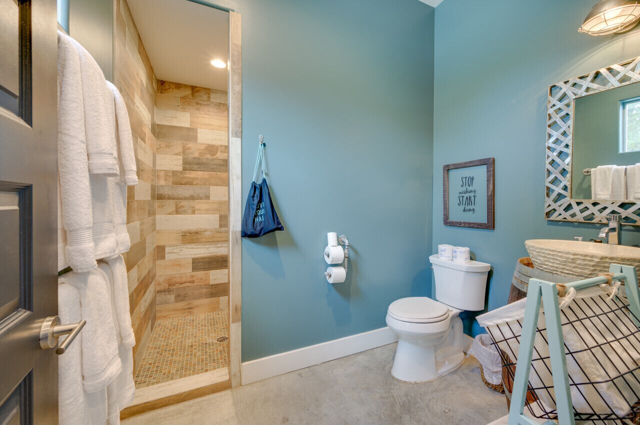 A bathroom with a shower, toilet, and sink. There are towels hanging on a rack and a blue bag hanging on the wall.