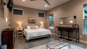 A bedroom with a bed, bedside tables, a desk, a chair, a ceiling fan, and a large window. - The Liney Moon (Dripping Springs)