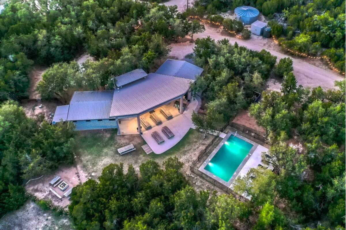 An aerial view of a house with a swimming pool, surrounded by dense greenery.