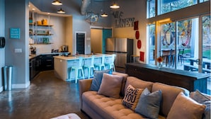 A modern kitchen with a central island, bar stools, and a dining area with a view of the outdoors. - The Liney Moon (Dripping Springs)