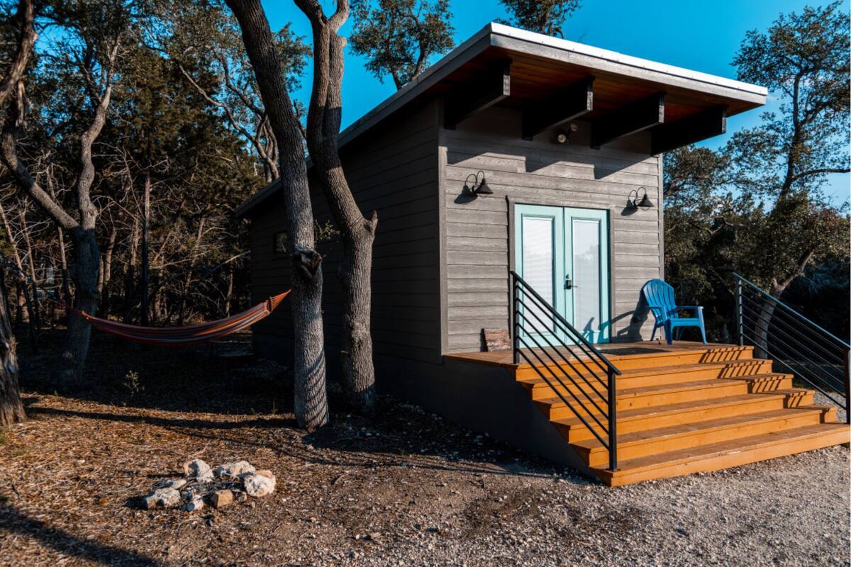 A cabin with a wooden deck, a hammock, and a staircase leading to a door.