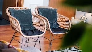 Deux fauteuils en osier avec des coussins foncés, dans une pièce dont le sol est en bois et qui est agrémentée d’un tapis à motifs.
