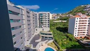 Un hôtel moderne à plusieurs étages, doté d’une cour intérieure avec une piscine et offrant une vue sur les collines environnantes.
