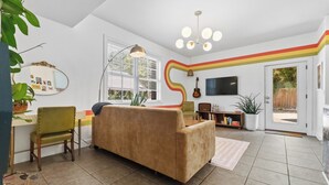 Een woonkamer met een bank, een eettafel, stoelen, een televisie en een raam met jaloezieën.