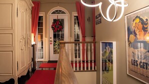 Een hotel lobby met een rode loper, een witte monumentale trap, een deur met een krans en een poster aan de muur.