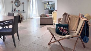 A spacious living area with a dining table, chairs, a sofa, and a chair with a blanket and hat.