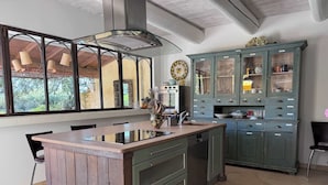 A kitchen with a central island, green cabinets, and a window with a view of greenery.