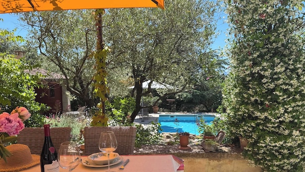 An outdoor dining area with a table set for two, a bottle of wine, and a view of a swimming pool.
