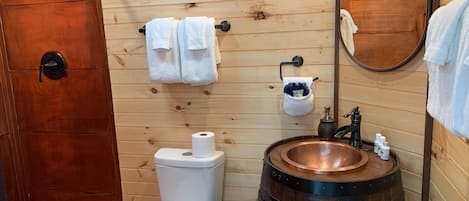 Un baño con paneles de madera, un inodoro, un lavamanos en forma de barril de madera y un espejo.