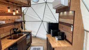 A compact kitchen with wooden cabinetry, a sink, a stove, and a coffee maker. - Moonshiner Tree Dome is rustic luxury with big, beautiful panoramic views. (Hico)