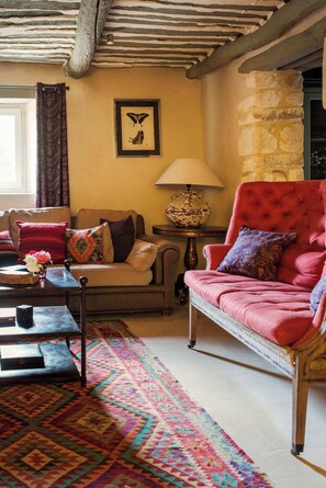 Un salón acogedor con un sillón rojo, un tapete estampado, una lámpara de estilo vintage y una obra de arte con una mariposa enmarcada en la pared.