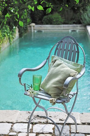 En metallstol med en kudde och ett glas vatten bredvid en pool.