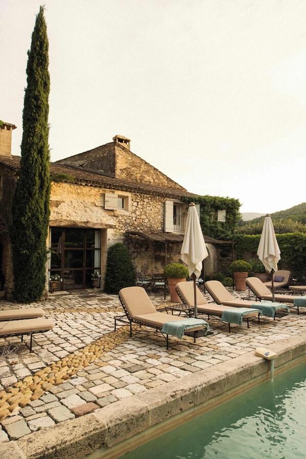 A stone building with a pool, lounge chairs, and umbrellas.