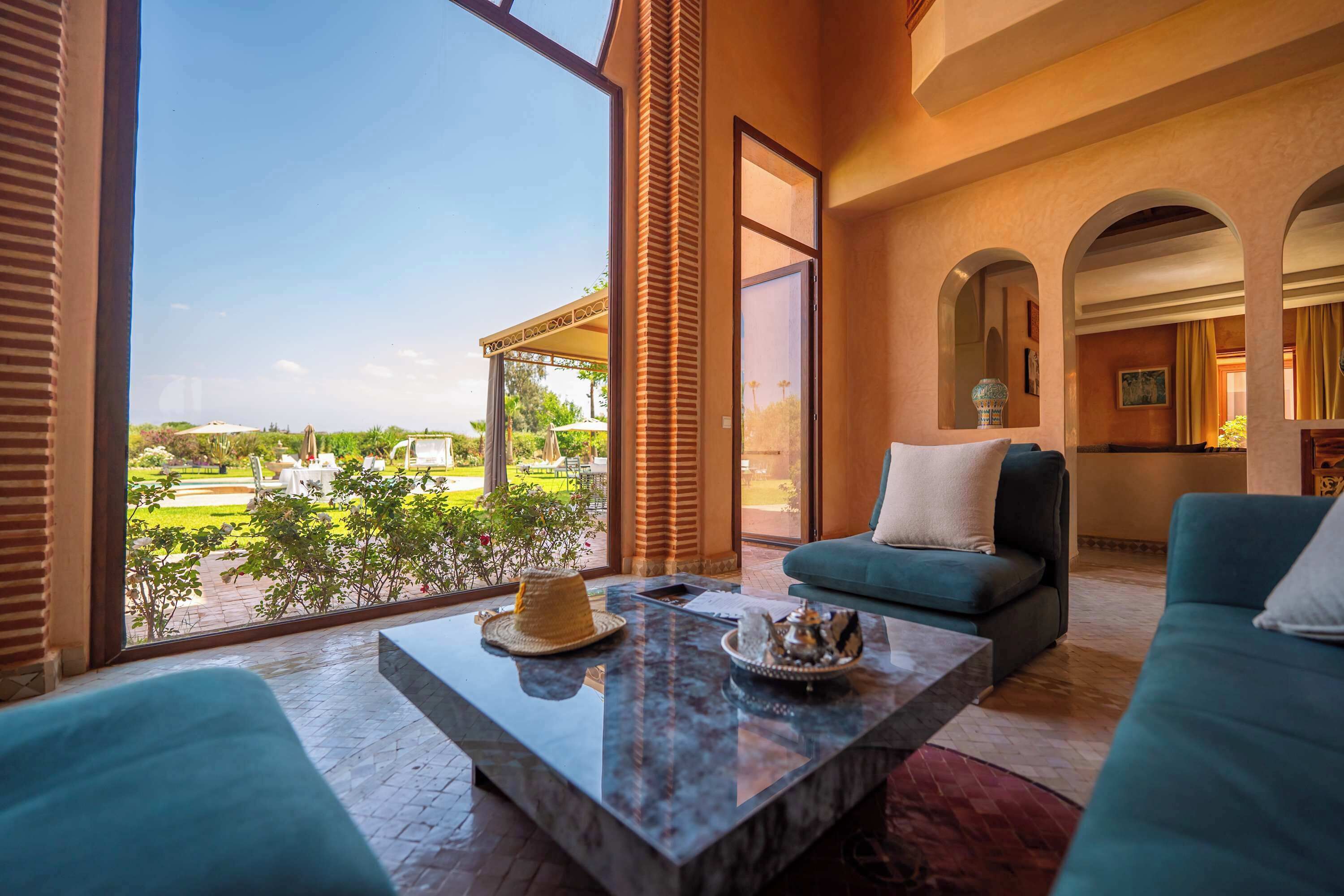 A spacious living area with a large window overlooking a garden, a marble coffee table, and a sofa with cushions.
