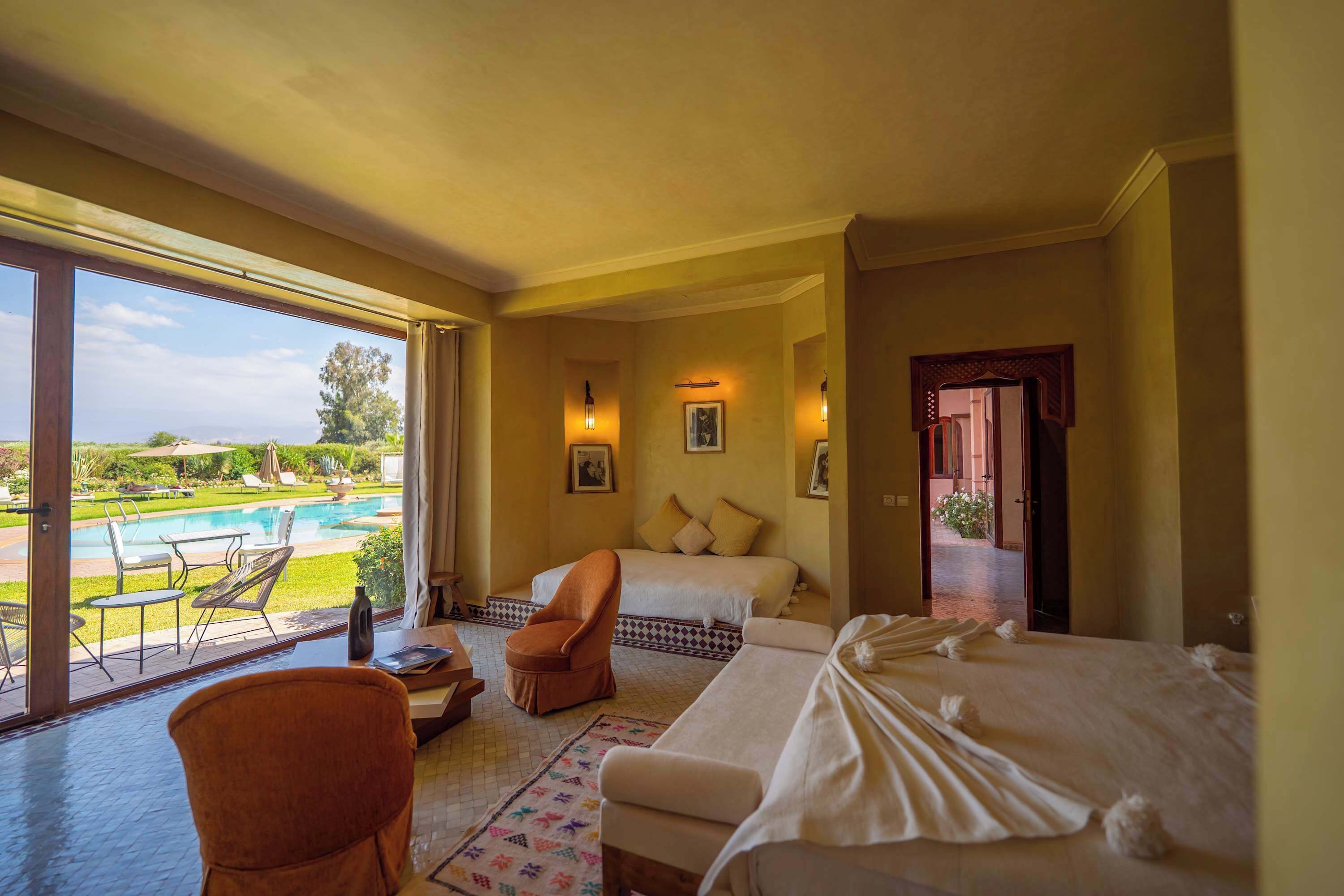 Camera d'albergo con un letto, una sedia, un tavolino, vista su una piscina e una porta che dà su un'altra stanza.