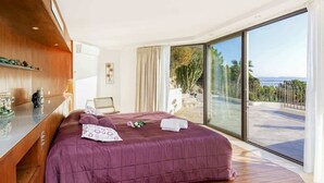 Une chambre à coucher moderne avec un grand lit, une commode en bois et un balcon offrant une vue sur la mer.