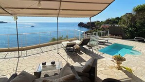 A covered outdoor area with a pool, lounge chairs, and a view of the sea. - Private beach villa, sea view (Théoule-sur-Mer)