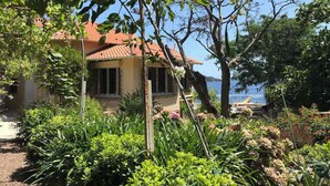 A house with a red-tiled roof, surrounded by lush greenery and a view of the sea. - Private beach villa, sea view (Théoule-sur-Mer)