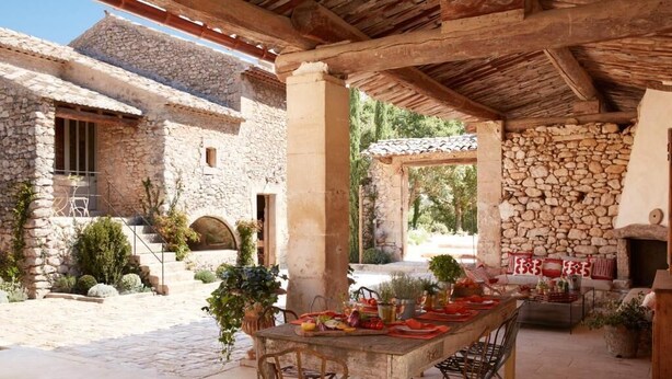 Un espace de restauration extérieur rustique, agrémenté de murs en pierre, d’une cheminée en pierre et d’une pergola.