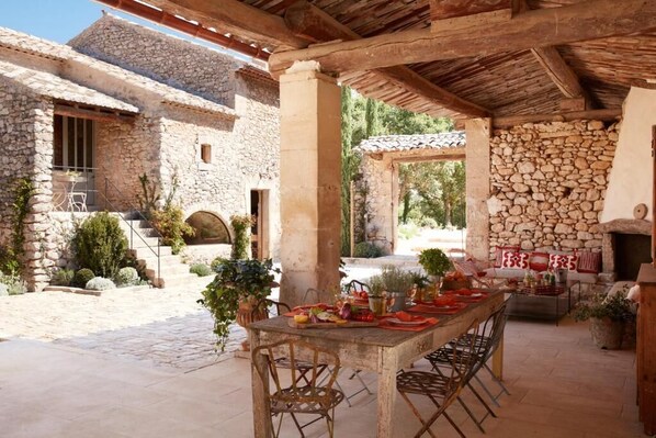 A rustic outdoor dining area with stone walls, a stone fireplace, and a pergola.