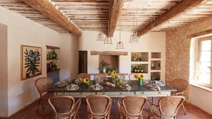 Une salle à manger rustique avec une longue table dressée pour six personnes, entourée de chaises en osier.