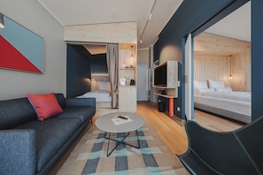 Una habitación de hotel moderna con sofá, una mesita redonda, una cama y televisión.