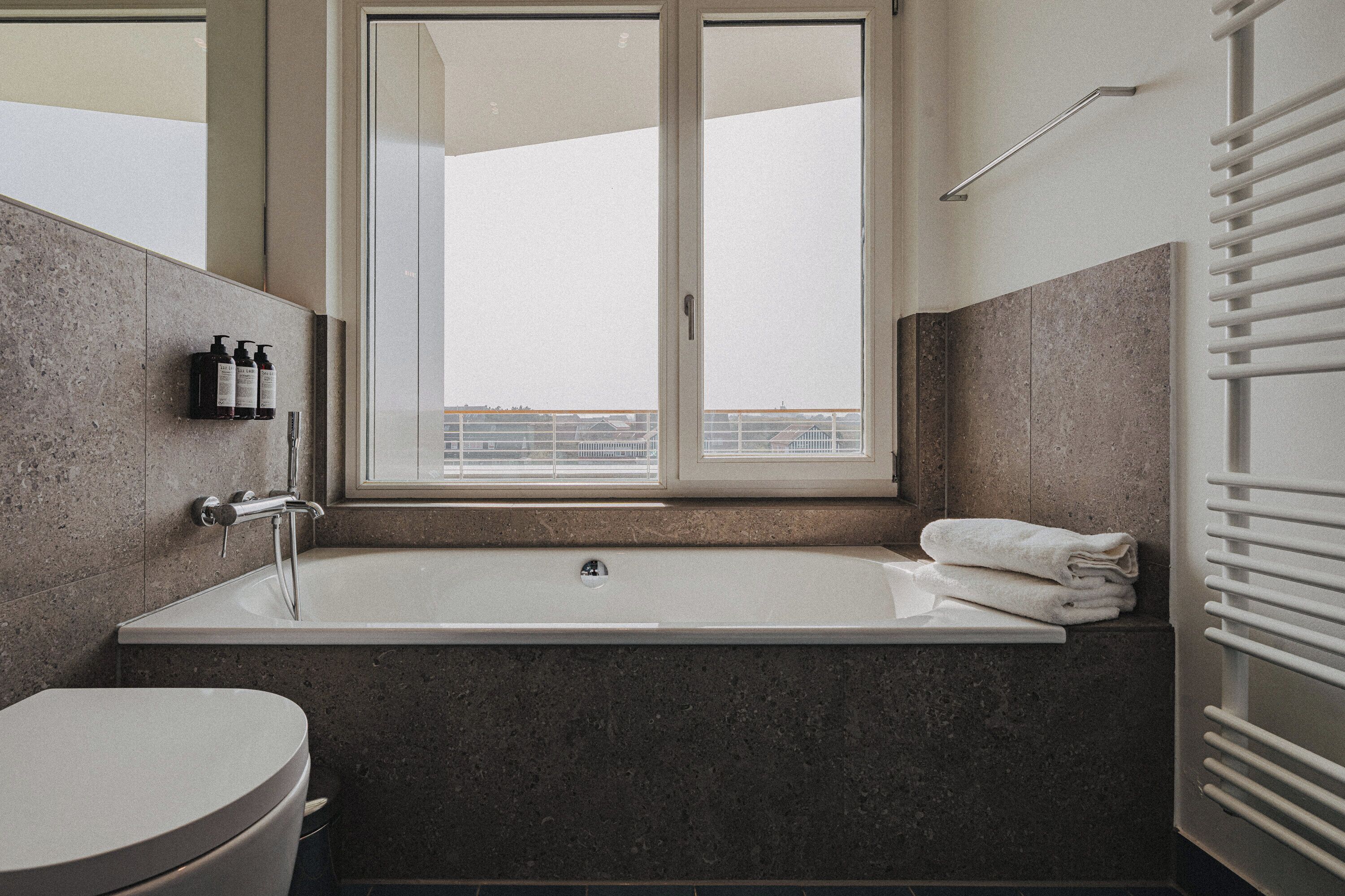 A modern bathroom with a bathtub, a toilet, and a window providing a view.