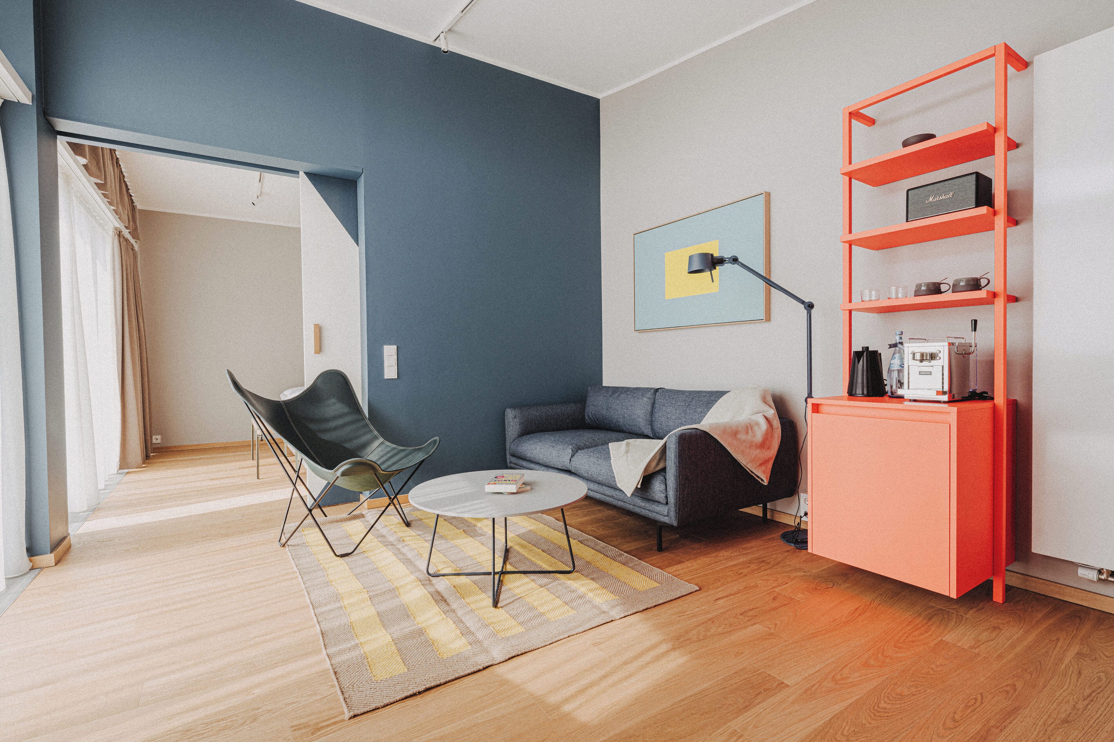 En moderne stue med sofa, stol, sofabord og et rødt reolsystem.