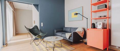 En moderne stue med sofa, stol, sofabord og et rødt reolsystem.