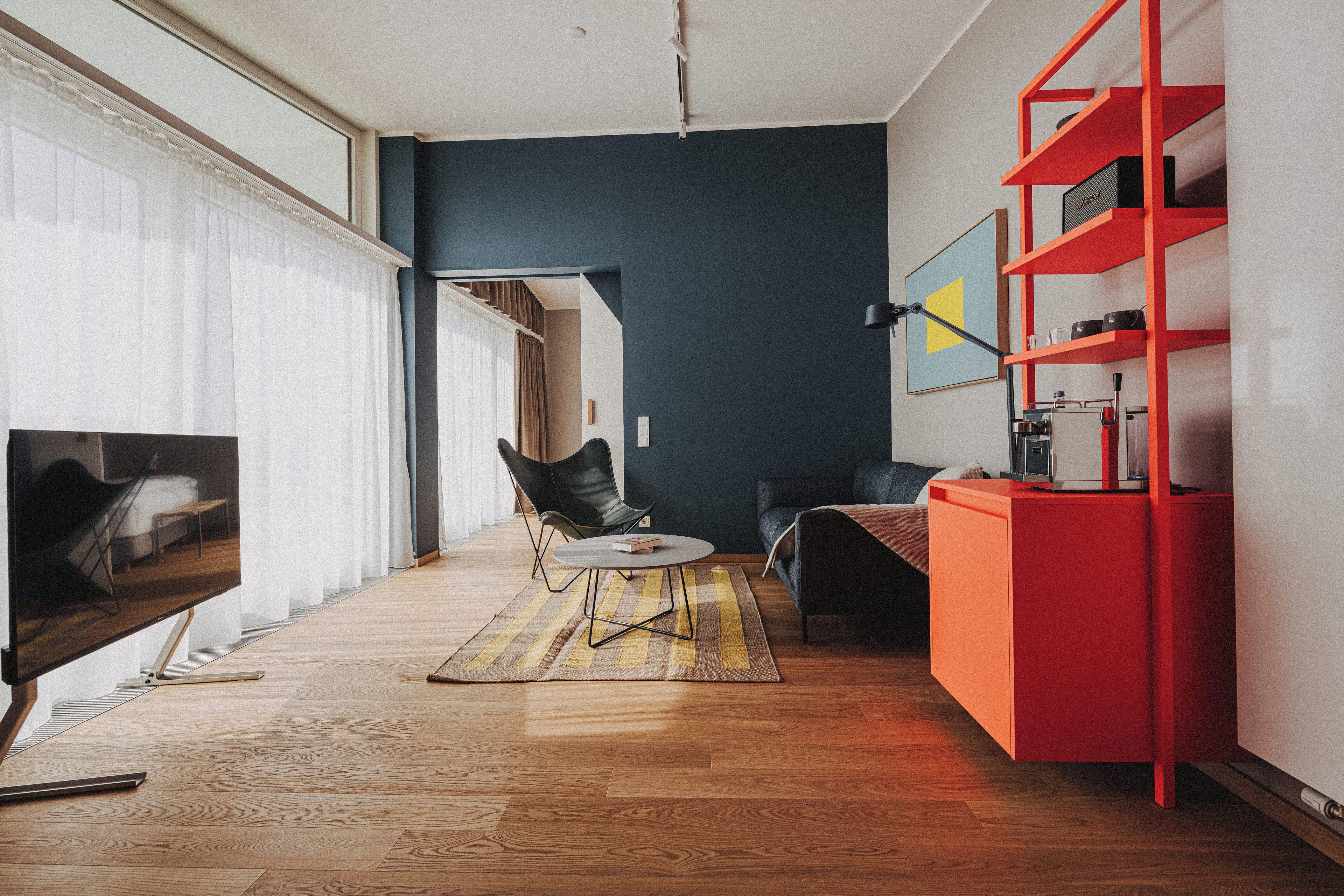 A modern living room with a large flat-screen TV, a sofa, a coffee table, and a red shelving unit.