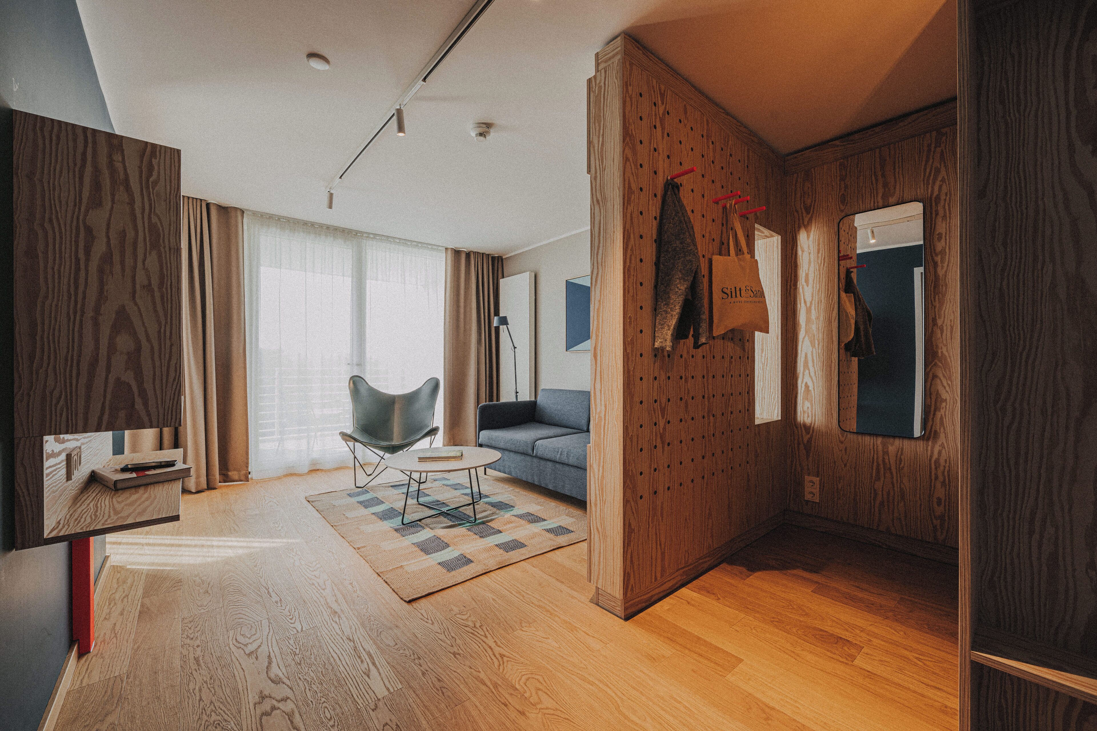 A modern hotel room with a wooden panel wall, a sofa, a small round table, and a chair.