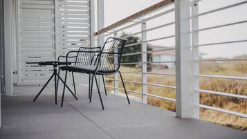 Ein Balkon mit zwei Stühlen, einem Tisch, weißen Geländern und Blick auf ein Feld.