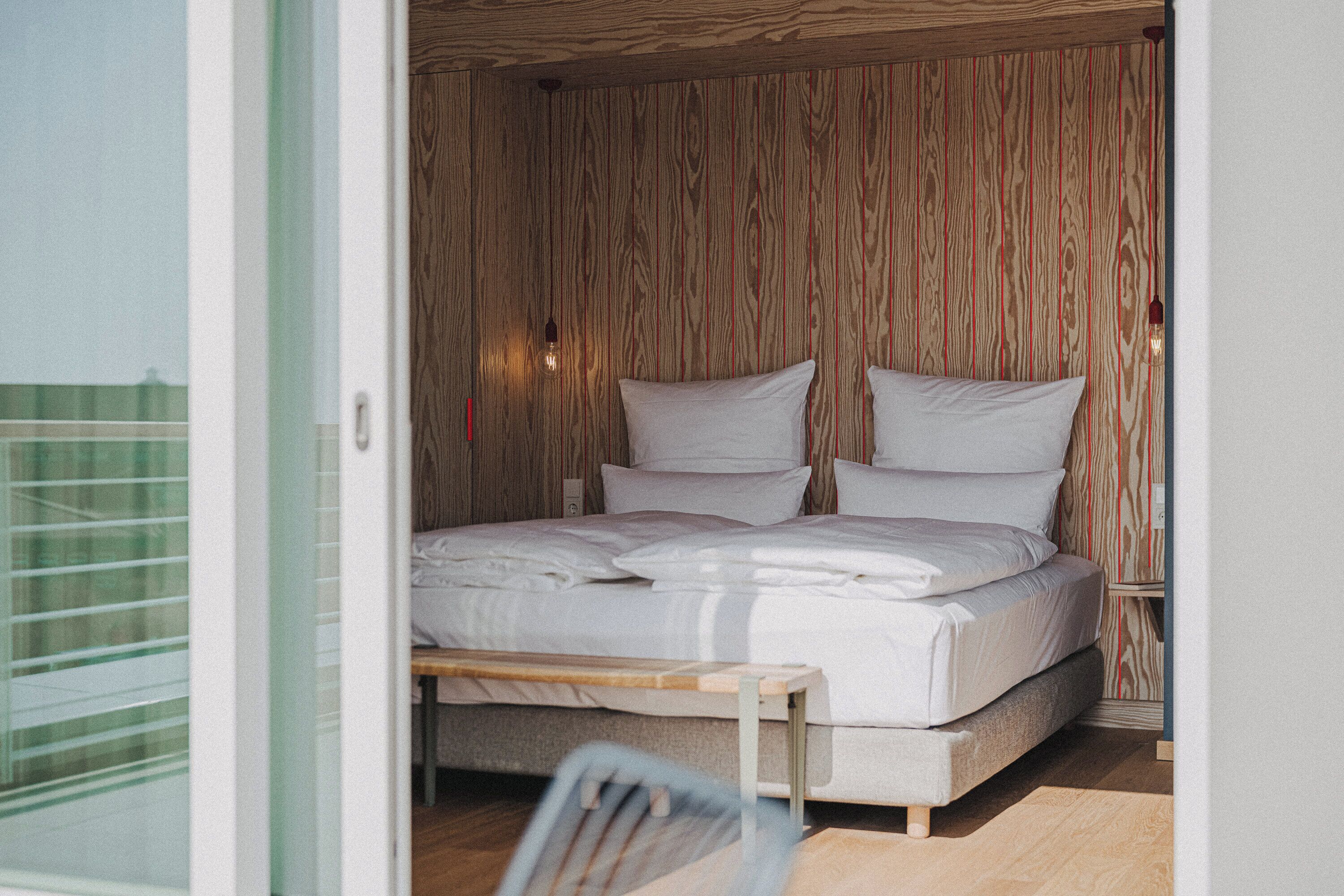 A bedroom with a wooden slatted wall, a bed with white bedding, and a nightstand with a lamp.