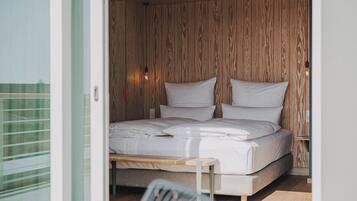 Quarto com parede de ripas de madeira, cama com roupa de cama branca e mesa de cabeceira com abajur.