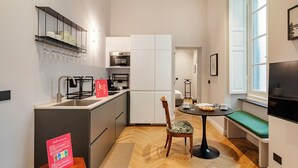 A compact kitchen with modern appliances, a dining area with a bench, and a large window providing natural light. - Corvetto Luxury Suite by Wonderful Italy (Genoa)