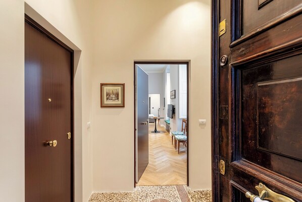 A hallway with a wooden door on the left, a framed picture on the wall, and a view into a dining area with a table and chairs.