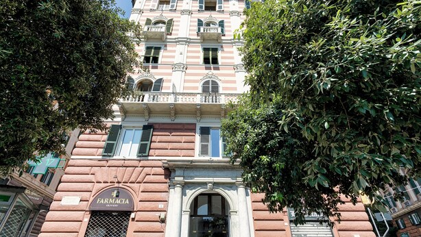 A building with a prominent pharmacy sign, a large arched entrance, and a balcony with railings. - Corvetto Luxury Suite by Wonderful Italy (Genoa)