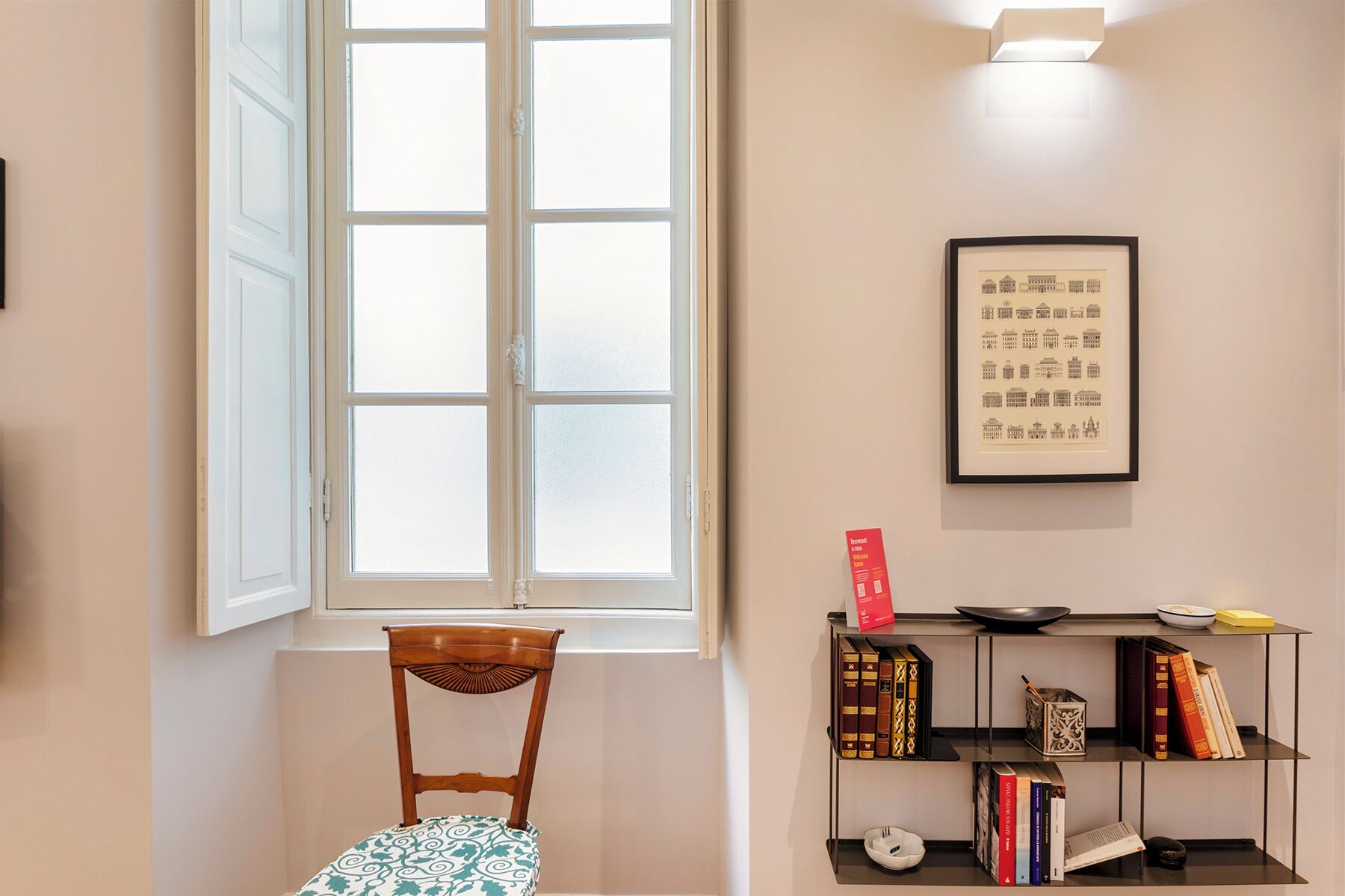 Une pièce avec une chaise en bois, une bibliothèque remplie de livres, un tableau encadré au mur et une fenêtre donnant sur un paysage.